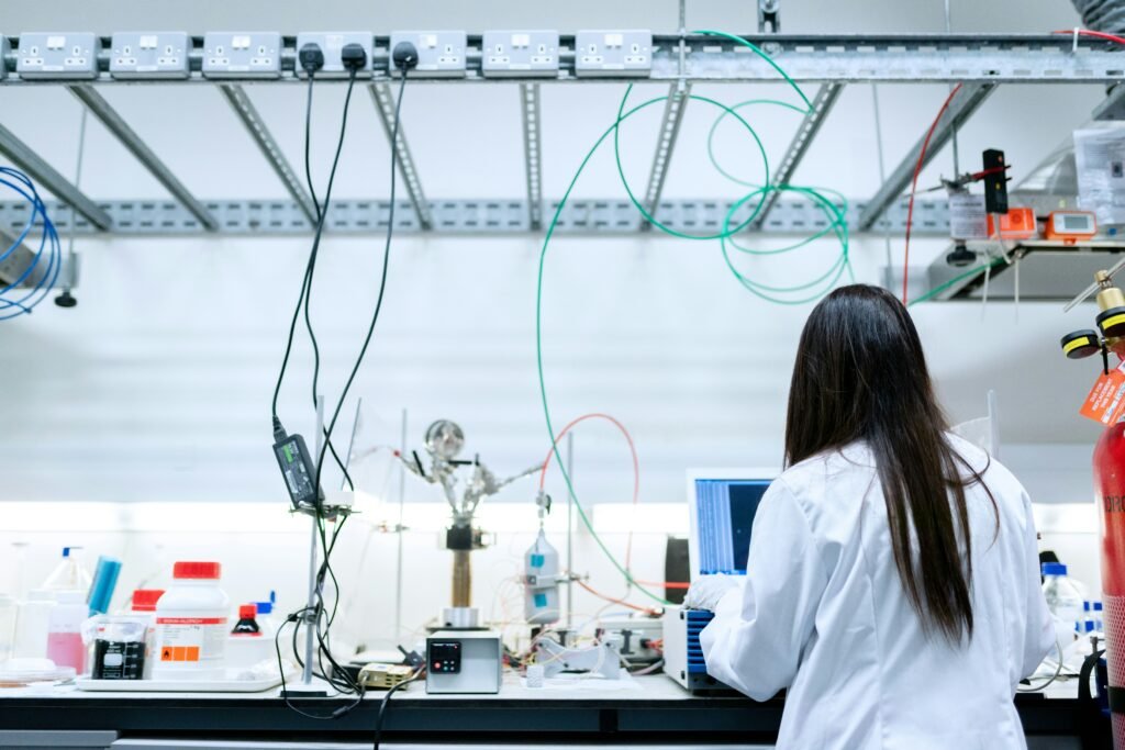 Researcher in a white lab coat working at a laboratory bench with a laptop and scientific equipment.